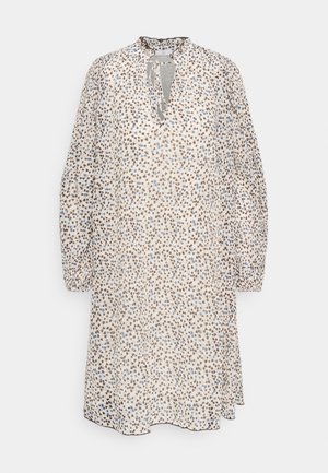 Luźna sukienka z długim rękawem sięgająca do kolan, w jasnobeżowym kolorze z małymi, brązowymi i niebieskimi abstrakcyjnymi plamkami, z falbankowym kołnierzem i wiązaniem przy szyi.