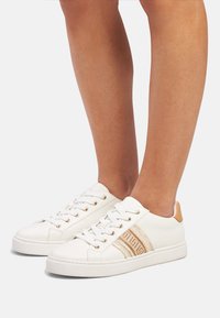 White leather sneakers with beige accents, featuring gold eyelets, a patterned side stripe, and textured back panel.