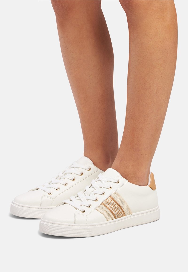 White leather sneakers with beige accents, featuring gold eyelets, a patterned side stripe, and textured back panel.