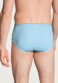 Lichtblauwe katoenen slips met een zachte textuur, een elastische tailleband en een aansluitend ontwerp, die een achterkant van het kledingstuk laten zien.