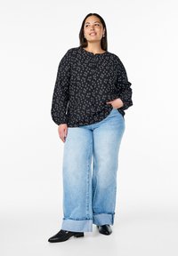 Blusa nera a fantasia con scollo rotondo e maniche lunghe, abbinata a jeans a gamba larga blu chiaro e scarpe col tacco nere.