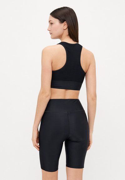 Μαύρο αθλητικό σουτιέν με υφή διαπλεκόμενου σχεδίου και απαλό λάστιχο, συνδυασμένο με μαύρα κολάν ποδηλασίας υψηλής μέσης που αγκαλιάζουν το σώμα.