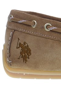 Braunes Wildleder-Schuhwerk mit beigem Gummisohle, ausgestattet mit weißen Nähten und schnürbarem Oberteil. Auffälliges geprägtes Polo-Spieler-Design an der Seite.