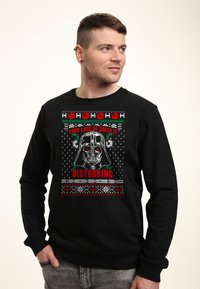 Uomo che indossa una felpa nera con il casco di Darth Vader e la scritta rossa "La tua mancanza di gioia è inquietante" in un design a tema natalizio.