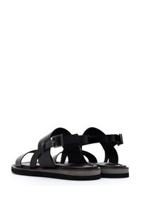 Black leather sandals with overlapping straps, adjustable buckles, a flat sole, and a subtle contrasting light gray trim.