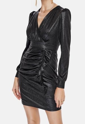 Zwarte mini-jurk met lange mouwen, V-hals, geplooide details en pofschouders, gedragen met gelaagde gouden kettingen en hangende oorbellen.