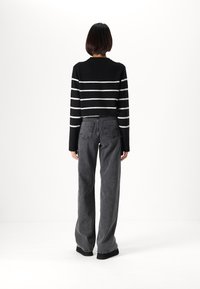 Suéter de punto a rayas en blanco y negro con mangas largas, combinado con jeans gris de pierna ancha de cintura alta. Diseño limpio y minimalista sin logotipos visibles.