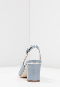 Sininen korkokenkä, jossa on sileä pinta, avoin takaosa ja koristeellinen solki. Lattiakorko on teksturoitu ja hieman kiiltävä.