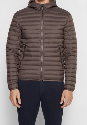 Bruine gewatteerde pufferjas met capuchon, ritssluiting aan de voorkant en ritssluitingen in de zijzakken, gedragen over een donkere broek door een staande persoon.