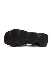 Semelle de chaussure en caoutchouc noir avec des motifs de bande de roulement profonds en zigzag et ondulés pour la traction, vue par en dessous sur fond blanc.