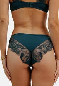 Ensemble de lingerie en teal avec des détails en dentelle transparente présentant des motifs floraux. La découpe au dos est de taille moyenne avec un tissu doux et lisse.