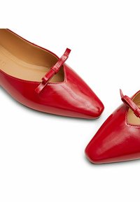 Scarpe in vernice rossa con punta appuntita, dotate di un piccolo fiocco vicino all'apertura e di un rivestimento interno liscio.