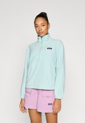 Pulover din fleece albastru deschis, cu guler ridicat și design cu fermoar pe jumătate. Are o mică patch logo pe piept și manșete elastice.