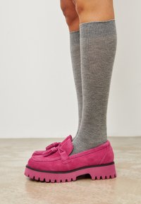 Rosa Wildleder-Loafers mit einer Quasten-Akzent, dicke Gummisohle und strukturierten Oberfläche, kombiniert mit grauen knielangen, gerippten Socken.