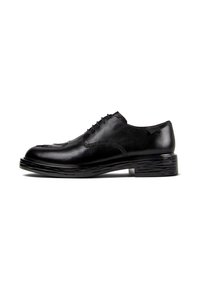 Scarpa elegante in pelle lucida nera con punta tondeggiante, chiusura a lacci e tacco basso texturizzato, mostrata in profilo laterale su sfondo bianco.