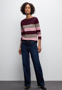 Gebreide trui in bordeauxrood met roze en grijze strepen; ronde halslijn, lange mouwen. Draag het met een donkerblauwe flared jeans en bruine laarzen.