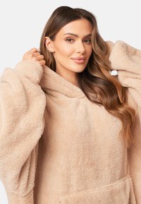 Fleece beige oversize con cappuccio, dal texture morbido e maniche ampie. Presenta una tasca frontale e un collo aderente.