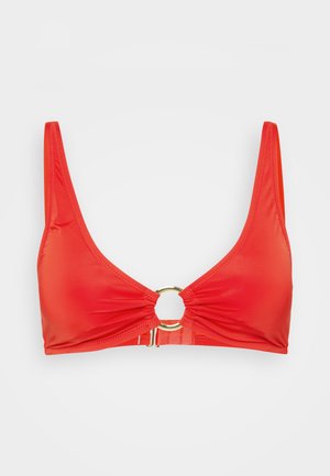 Rød bikinitopp med dyp V-hals, tynne stropper, samlet stoff i midten, og en gullsirkelf ornament ved bysten. Glatt tekstur.