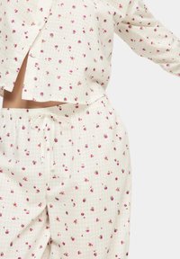 Set di pigiama in cotone caratterizzato da uno sfondo bianco con piccoli motivi floreali rosa. La maglietta ha una vestibilità comoda e una chiusura con bottoni, mentre i pantaloni corti hanno una fascia elastica in vita con un cordoncino.