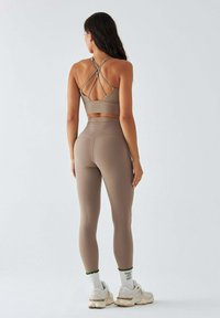 Komplet stanika i legginsów w miękkim taupe. Biustonosz posiada krzyżujące się ramiączka, a legginsy z wysokim stanem idealnie dopasowują się do sylwetki.