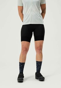 Shorts de cyclisme noirs en tissu texturé, haut zippé gris à manches courtes, chaussettes bleu marine à motifs, associés à des chaussures de cyclisme noires.