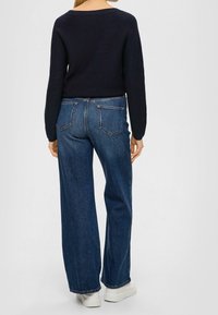 Marinblå stickad tröja med båturringning i kombination med högmidjade, vida mörkblå jeans. Vita skor fulländar outfiten.