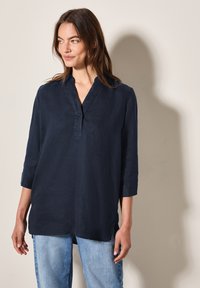 Camicia di lino blu navy con colletto e patta bottonata, dotata di maniche a tre quarti e vestibilità rilassata. Tessuto testurizzato con spacco laterale.
