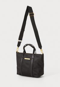 Mustat nylon-kassi nahka-aitoilla. Ominaisuuksiin kuuluu kaksoiskahvat, irrotettava olkahihna ja kultasävyinen logolaatta.