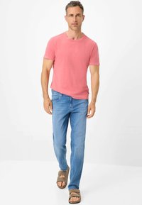 T-shirt a maniche corte di colore corallo rosa abbinata a jeans azzurri chiari e sandali scivolati marroni, caratterizzata da una vestibilità comoda e un design semplice.