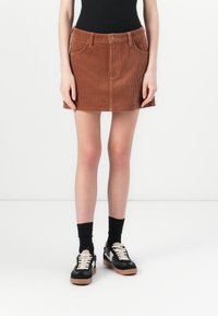 Brown corduroy mini skirt with front pockets, belt loops, and a button closure. Paired with black socks and sneakers.