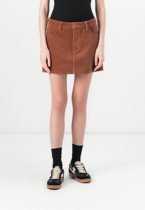 Brown corduroy mini skirt with front pockets, belt loops, and a button closure. Paired with black socks and sneakers.