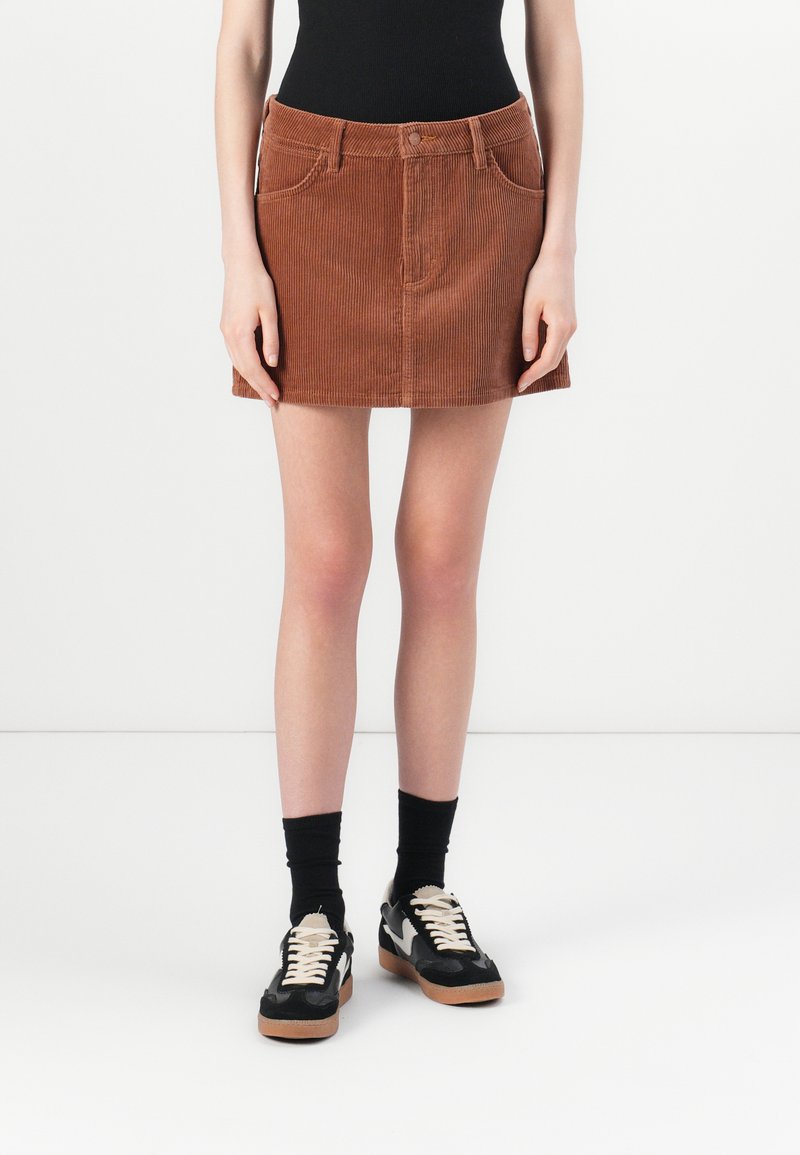 Brown corduroy mini skirt with front pockets, belt loops, and a button closure. Paired with black socks and sneakers.