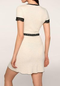 Z dzianinowa sukienka w jasnym beżu z czarną koronką wykończoną na rękawach i w pasie, z dopasowaną górą i rozkloszowanym dołem.