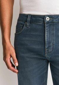 Dunkelblaue Jeans aus Denim mit geradem Schnitt, ausgestattet mit Knopfverschluss, Fünf-Taschen-Design und dezenten Nahtdetails.