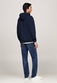 Sudadera azul marino con capucha ajustable, puños y dobladillo acanalados, combinada con jeans oscuros de pierna recta y zapatillas blancas.