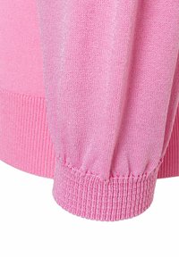 Pull en tricot rose avec des poignets et un ourlet côtelés. Le tissu a une texture lisse avec une légère brillance. Détails de couture soignés.