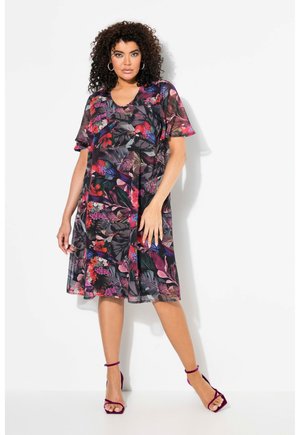 Vestido floral de tela negra transparente con vibrantes patrones rojos y morados. Mangas cortas, corte suelto y silueta relajada, combinado con tacones morados.