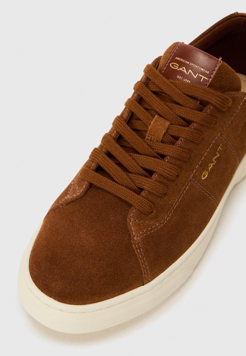 Brązowe zamszowe sneakersy z tonacjami sznurówek, z kremową gumową podeszwą i złotą wypukłą metką logo na języku.