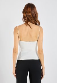 White camisole with thin spaghetti straps, fitted design, and smooth texture; paired with black wide-leg pants.