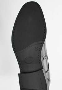 Semelle de chaussure en cuir noir avec une finition lisse, présentant des accents en caoutchouc texturé et des coutures décoratives le long des bords.