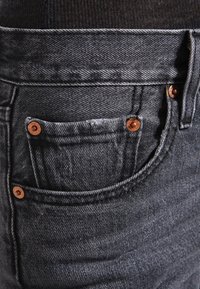 Musta denimitakki kuparinastoilla, jossa on pieni etutasku ja teksturoitu kangas. Saumojen kohdalta näkyvät tikit.