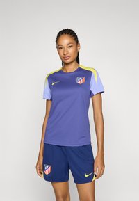 Lila atletisk tröja med ljusblå ärmar och gula detaljer, med en klubb-logotyp på bröstet. Matchas med marinblå shorts.