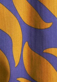 Tessuto viola con un motivo ondulato arancione, caratterizzato da una superficie liscia e da una leggera lucentezza che illumina i dettagli del design.