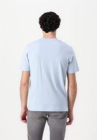 Tricou din bumbac bleu deschis, cu mâneci scurte, design cu guler rotund, textură netedă, expus din spate, cu pantaloni gri.