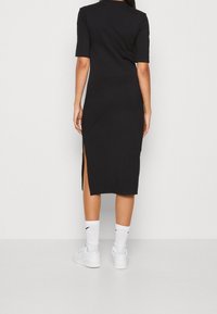 Svart midi-klänning med korta ärmar, sidofickor och en avslappnad passform. Materialet är glatt och stretchy, kombinerat med vita sneakers och ankelsockor.