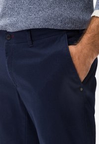 Granatowe bawełniane spodnie o fakturowanej tkaninie, z bocznymi kieszeniami, zapięciem na guziki oraz widocznymi przeszyciami dekoracyjnymi.