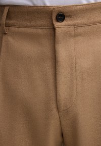 Brązowe spodnie z mieszanki wełny o gładkiej fakturze, z pojedynczym zapięciem na guzik oraz dopasowanym przodem z płaskim krojem i starannym wykończeniem szwów.