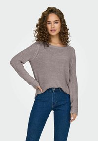 Pull en tricot gris clair avec une coupe décontractée et un col rond, associé à un jean taille haute bleu foncé. Tissu texturé, manches longues.