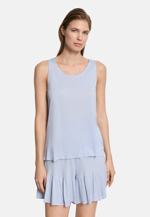 Donna con capelli castano chiaro, indossa una canottiera azzurra senza maniche e pantaloncini arricciati abbinati, su sfondo bianco neutro.