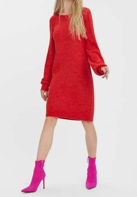 Robe-pull rouge à manches longues avec une coupe décontractée et des poignets côtelés, associée à des bottines à talons aiguilles roses avec des fermetures éclair latérales.